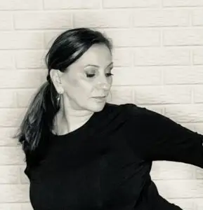 Lisa in a yoga pose against a light brick wall, wearing a black top, looking calm and focused.